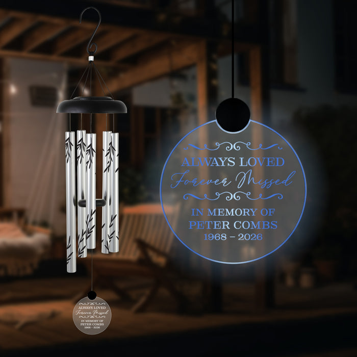 memorial solar garden wind chime with name and years of life hanging in the dark in front of a wooden bench