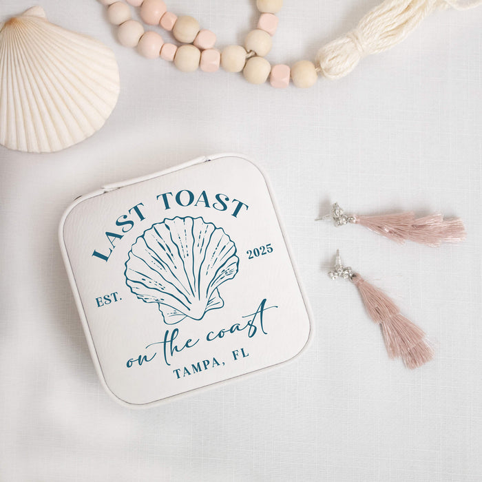 White jewelry box with shell design and text on a light background with decorative items.
