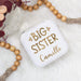 Small white jewelry box with 'Big Sister' text on a light background with wooden beads.