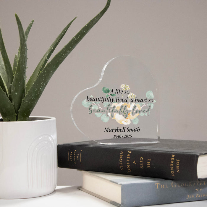 Heart-shaped personalized memorial plaque on books with a plant in the background