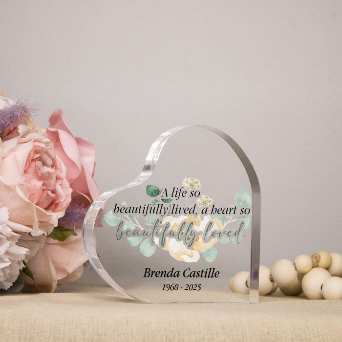 Heart-shaped glass plaque with printed text and floral design, placed on a surface with flowers and beads.