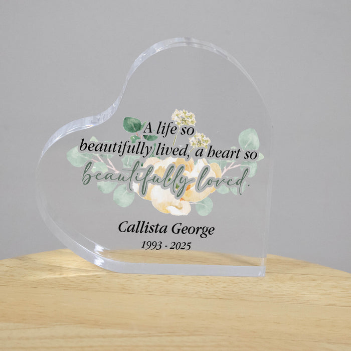 Heart-shaped glass plaque with floral design and text on a wooden surface.
