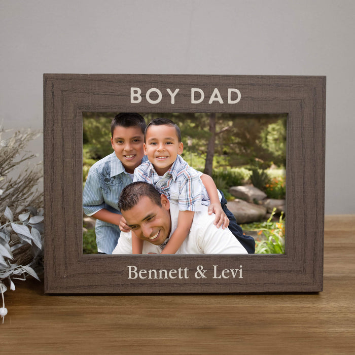 Wooden photo frame with 'BOY DAD' and personalized names on a wooden surface.