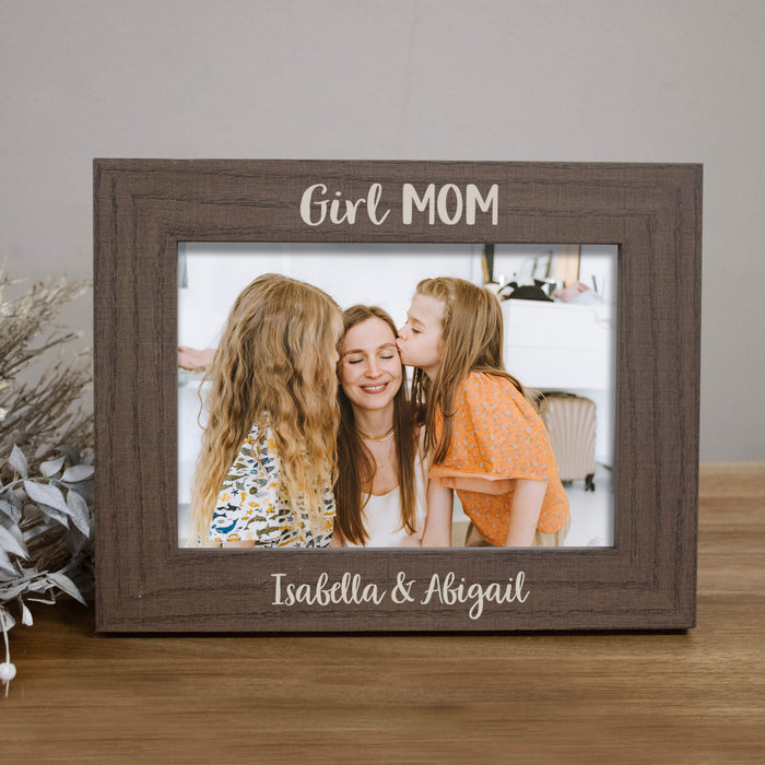 Brown wooden photo frame with 'Girl MOM' and names 'Isabella & Abigail' on a wooden surface.