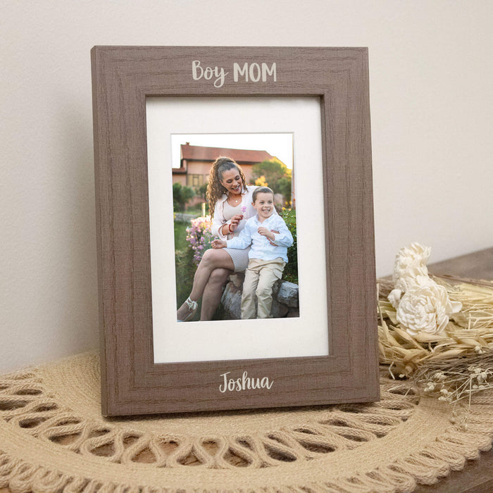 Wooden photo frame with a picture of a woman and child, resting on top of a placemat next to dried floral