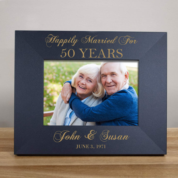 Black frame with gold text 'Happily Married For 50 Years' and a photo of an elderly couple, placed on a wooden surface.