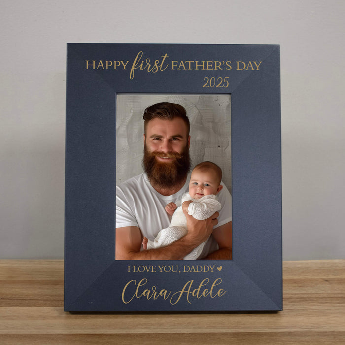 Black photo frame with a father and child photo, text 'Happy first Father's Day 2025' and 'I love you, daddy' on a wooden surface.