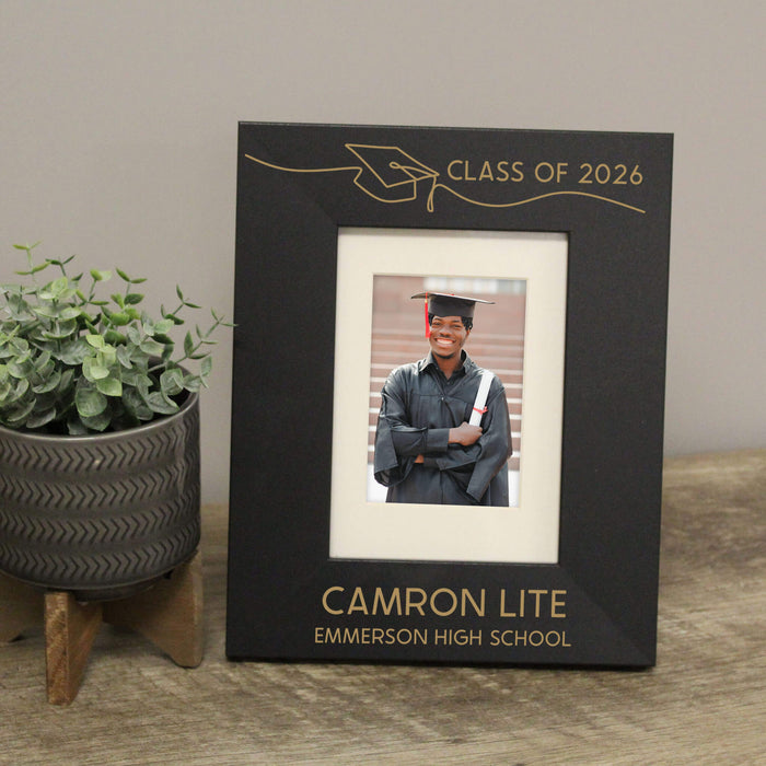 Graduation-themed photo frame with a picture of a graduate, placed on a surface with a plant in the background.