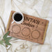 A personalized wooden cookie tray with gold-toned handles and engraved text reading 'Santa's Cookies' and three circular areas, styled on a cream knit blanket with a white coffee cup and a small green leaf sprig.