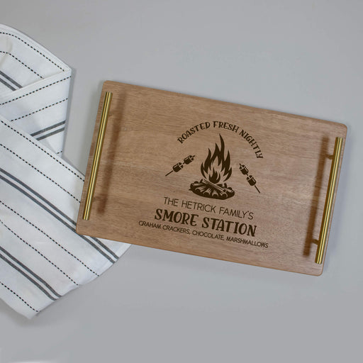 Wooden serving tray with engraved text "S'more Station" and campfire design on a gray surface
