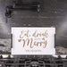 A white rectangular serving tray with black side handles sits on a gas stovetop in a kitchen. The tray has an engraved design with the phrase 'Eat, drink and be Merry' in brown script and serif fonts, along with the personalized name 'THE NELSONS' at the bottom.