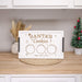 A personalized white Christmas cookie tray engraved with 'Santa's Cookies' and three circular spaces, displayed on a wooden countertop in a kitchen setting with a small Christmas tree and dried grass in the background.