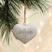 A personalized white heart-shaped Christmas ornament hanging from a pine tree branch with warm string lights in the background. The ornament is engraved with the name 'The Grahams' and an established year.