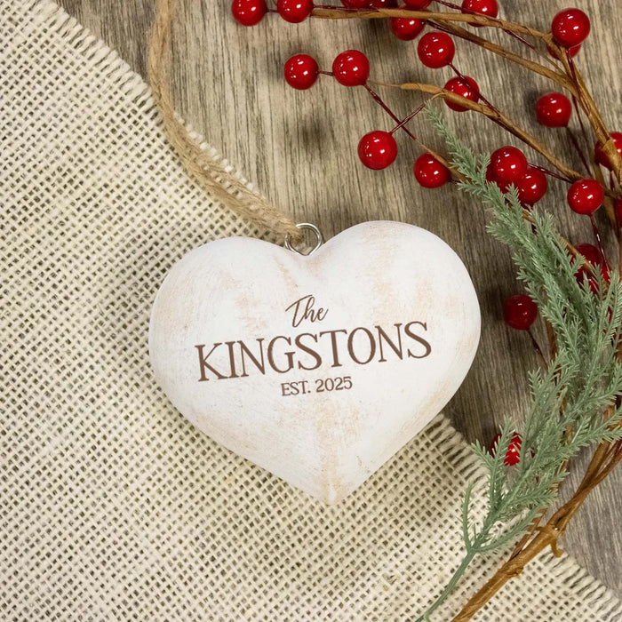 A heart-shaped wooden ornament with a rustic distressed finish, engraved with the text 'The KINGSTONS EST. 2025' in brown lettering.