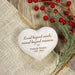 Personalized heart-shaped wooden keepsake ornament with engraved text 'Loved beyond words, missed beyond measure. Pamela Ramer 1952 - 2025', hanging on a rustic wood surface with burlap, red berries, and greenery.