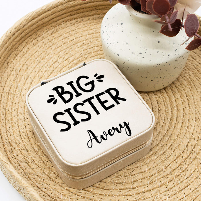 Small jewelry box with 'Big Sister' text on a woven surface with a vase in the background