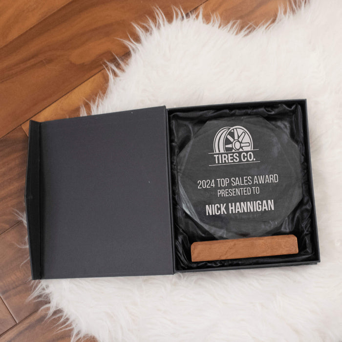 Decorative crystal plaque award with wooden base in a black box on a fluffy white rug.