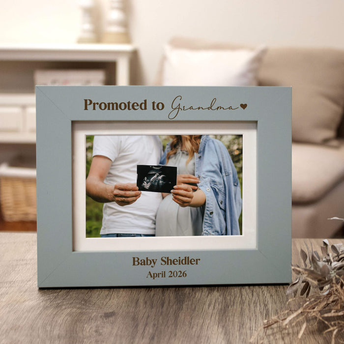 Horizontal light blue picture frame engraved with the phrase "Promoted to Grandma" in a living room setting