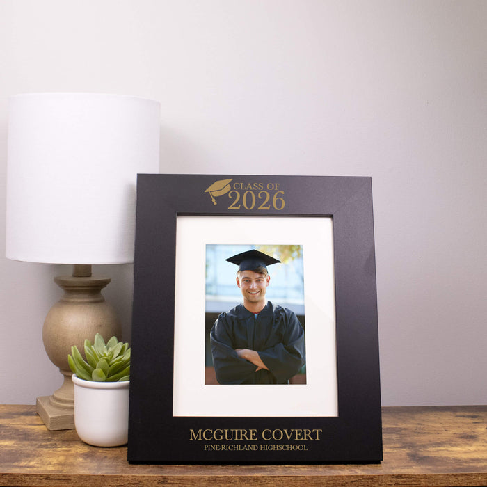 Graduation photo frame with a picture of a graduate on a wooden surface.