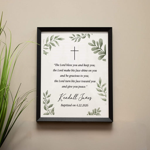 Framed print with religious text and cross design on a beige wall.