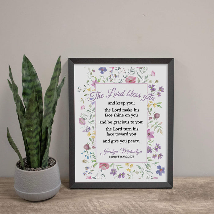 Framed print with floral design and text on a wooden surface next to a plant.
