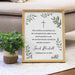Framed print with a cross and text on a surface next to a plant