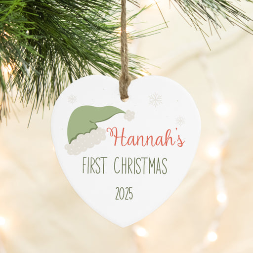 Heart-shaped ornament with 'Baby's First Christmas 2025' text, hanging on a Christmas tree.