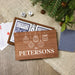A personalized wooden gift box set for dominoes, featuring a custom printed front lid with white text reading 'THE PETERSONS' and white line art of hanging ornaments. Inside, the dominoes and playing cards are visible.