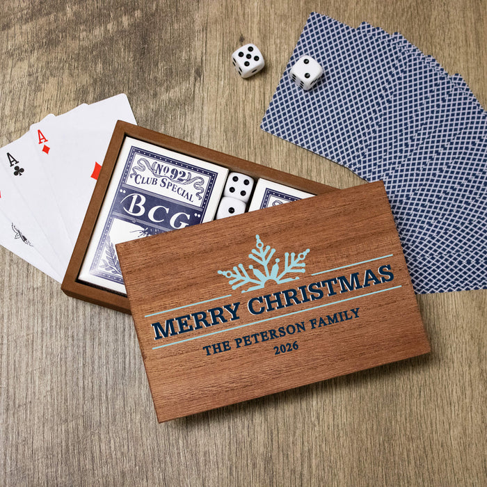 A personalized wooden Christmas card game box printed with 'MERRY CHRISTMAS' THE PETERSON FAMILY 2026 and a snowflake design, shown open with playing cards and dice on a wood surface.