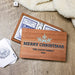 A personalized wooden Christmas gift box with a printed snowflake and the text 'MERRY CHRISTMAS' THE DAVIS FAMILY 2026, shown open with playing cards and dice on a wood surface with a cream blanket nearby.