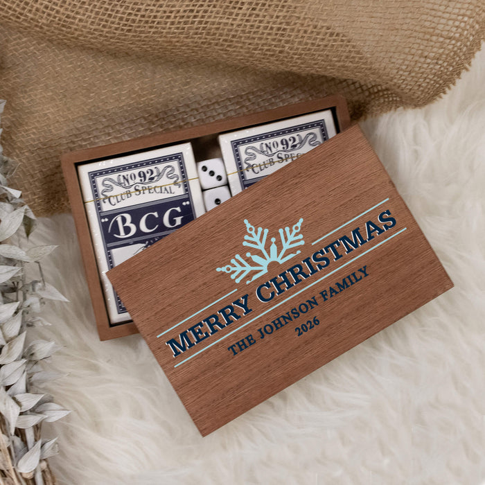 Personalized wooden Christmas-themed card game gift box with two playing cards visible inside, styled on a white faux-fur surface with burlap and dried flowers.
