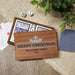 A personalized wooden Christmas card game box shown open on a woven mat with playing cards, dice, and a deck of cards nearby. The front of the box is printed with a snowflake and the text 'MERRY CHRISTMAS' THE AUDINO FAMILY 2026.