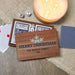Personalized wooden Christmas-themed card game box on a burlap surface next to a lit candle, playing cards, dice, and a blue patterned card back.