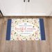 Decorative doormat with floral design and text on a wooden floor.