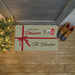 A personalized holiday doormat styled on a wooden porch floor next to a Christmas tree and a pair of boots. The doormat is green with white polka dots, featuring a red ribbon graphic, 'Merry Christmas' text, and 'The Chambers' printed in dark green script.