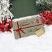 A personalized Christmas doormat in sage green with white polka dots, a red ribbon, and 'Merry Christmas The Ryans' printed on it, styled in a snowy porch setting next to poinsettias and a green door.