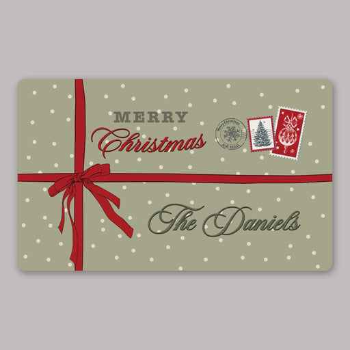 A Christmas-themed door mat with a sage green background, white polka dots, a red ribbon and bow, postage stamp graphics, and the text 'Merry Christmas' and 'The Daniels' on a plain gray background.