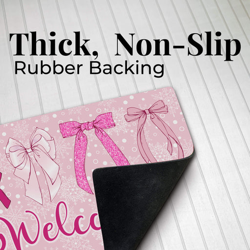 A pink welcome doormat with bow illustrations and the partial word 'Welcome' visible, shown on a white wood-plank background with large text reading 'Thick, Non-Slip Rubber Backing' and the back side peeling up to reveal a black rubber surface.