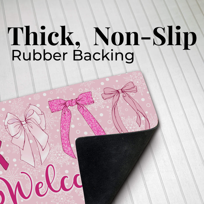 A pink welcome doormat with bow illustrations and the partial word 'Welcome' visible, shown on a white wood-plank background with large text reading 'Thick, Non-Slip Rubber Backing' and the back side peeling up to reveal a black rubber surface.