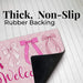 A pink welcome doormat with bow illustrations and the partial word 'Welcome' visible, shown on a white wood-plank background with large text reading 'Thick, Non-Slip Rubber Backing' and the back side peeling up to reveal a black rubber surface.