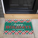 A personalized holiday doormat placed in front of a black front door on a concrete porch. The mat features a green center with the words 'happy HOLIDAYS' and the name 'THE THOMPSONS' in white, bordered by red, green, and white plaid patterns at the top and bottom.