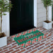 A personalized holiday doormat with a green background, red and green plaid borders, and the text 'happy HOLIDAYS THE NAMPTON' in white and red, placed on a brick porch in front of a black door.