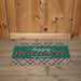 A rectangular holiday doormat with a green center, red and white plaid borders, and the words 'happy HOLIDAYS THE LEIGHTYS' in white and red, placed in front of a wooden door.
