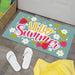 Decorative doormat with 'Hello Summer' text and strawberry design on a floor with white sandals and a yellow towel.