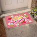 Pink doormat with 'Hello Summer' text and strawberry design on a concrete sidewalk.