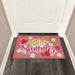 Pink doormat with 'Hello Summer' text and strawberry and flower designs on a wooden floor.