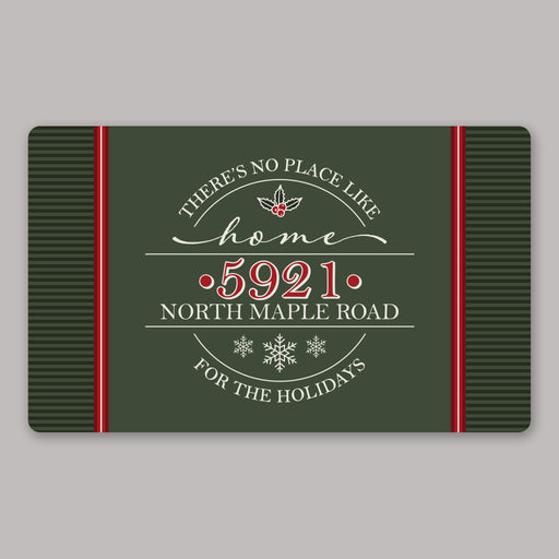 A rectangular holiday-themed door mat with a dark green background, red side panels, and white decorative text reading “There’s no place like home 5921 North Maple Road for the holidays,” centered on a light gray background.