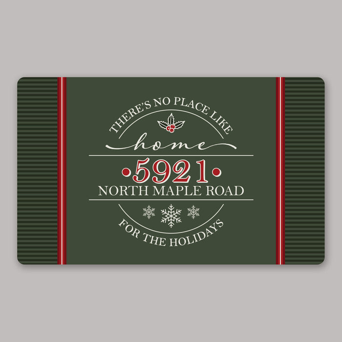 A rectangular holiday-themed door mat with a dark green background, red side panels, and white decorative text reading “There’s no place like home 5921 North Maple Road for the holidays,” centered on a light gray background.