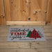 A personalized doormat with a holiday message and three Christmas tree designs in different patterns, placed on a wooden floor in front of a wooden door.