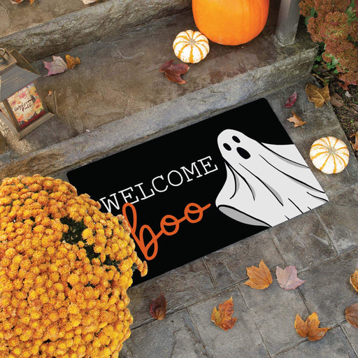 A black welcome mat that reads 'Welcome Boo', it has a ghost coming from the side of the mat. It is placed on cement stairs and surrounded by pumpkins and greens.
